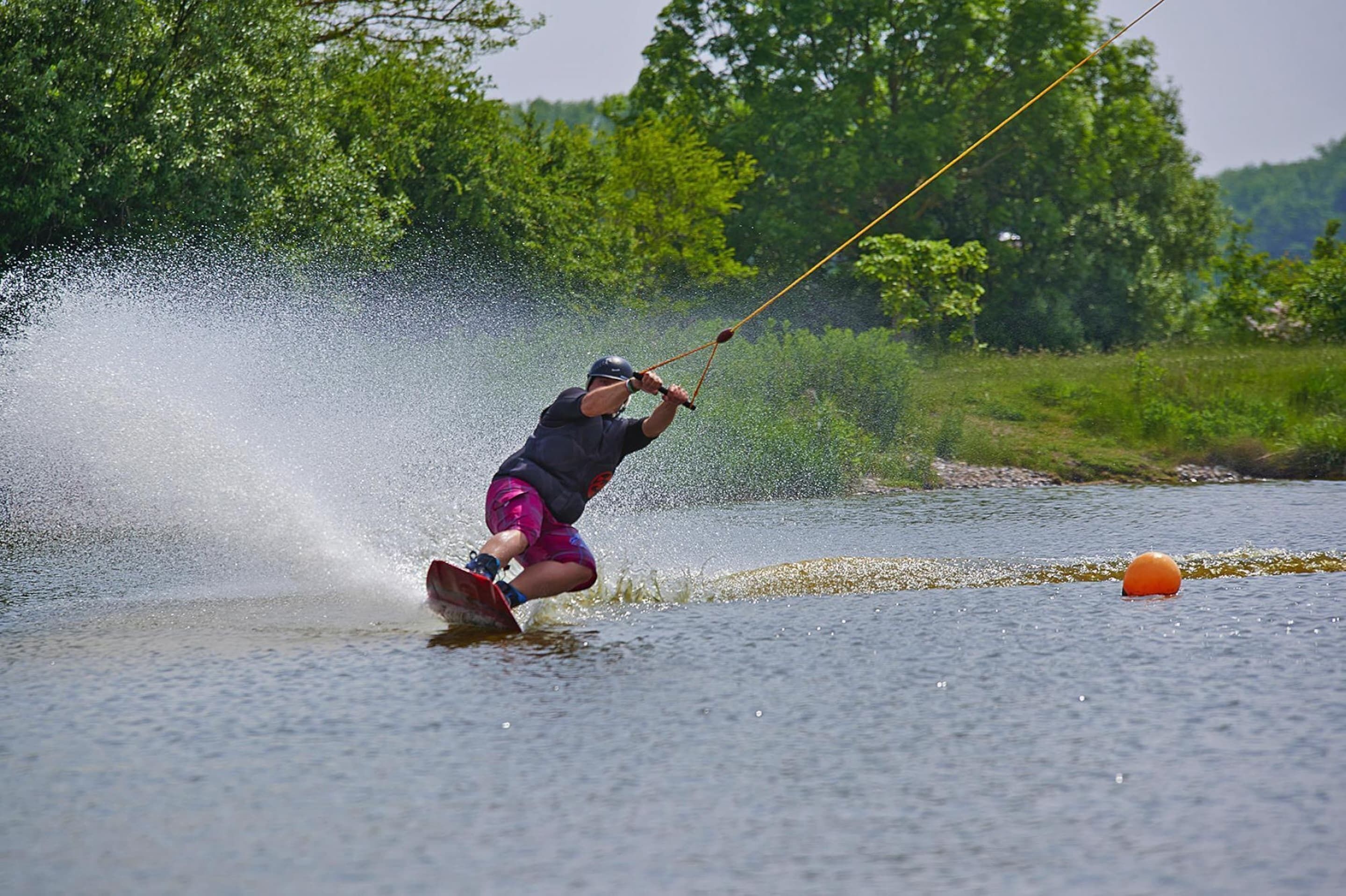 A person wakeboarding on a river, surrounded by greenery.
