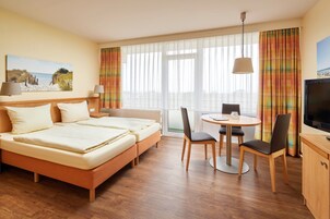 A hotel room with a bed, a desk, a chair, a TV, and a painting on the wall.