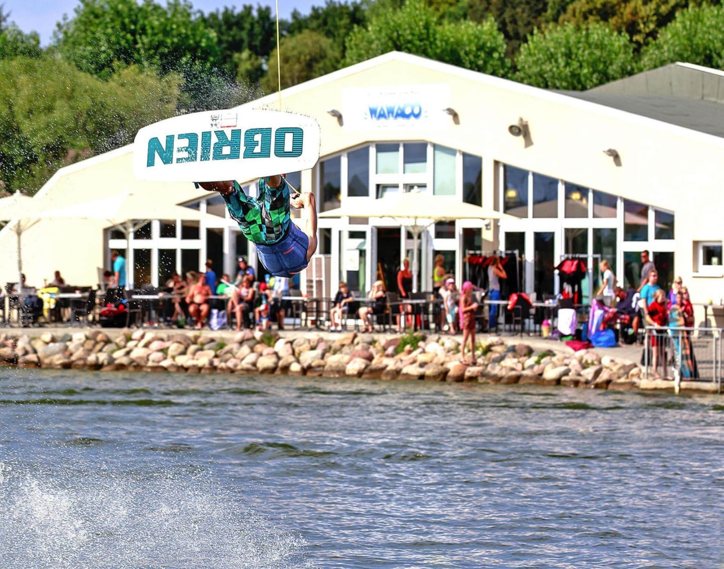A person performing a trick on a wakeboard in front of a building with a sign that reads "DORIN".