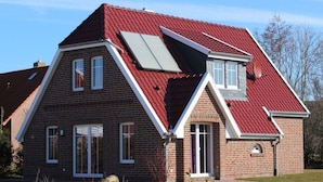 A two-story house with a red roof, a sloped front, and a small attached garage. - Ferienhaus in Dornum am Wasserschloss (Dornum)
