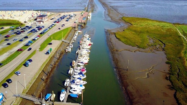 An aerial view of a coastal marina with parked cars and docked boats. - Ferienhaus in Dornum am Wasserschloss (Dornum)