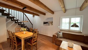 Un comedor con mesa y sillas de madera, una escalera, un sofá y un ventanal con vistas.