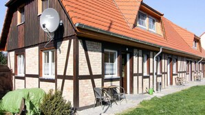 Una casa tradicional de entramado madera con techo rojo inclinado, una antena parabólica y un pequeño espacio exterior con mesas y sillas.