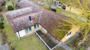 Ein Wohnhaus mit geneigtem Dach, einer Holzdiele und einem eingezäunten Garten.