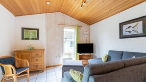 Ein gemütliches Wohnzimmer mit Holzbalkendecke, einem Fernseher, einem Sofa, einem Sessel und einem Schrank.