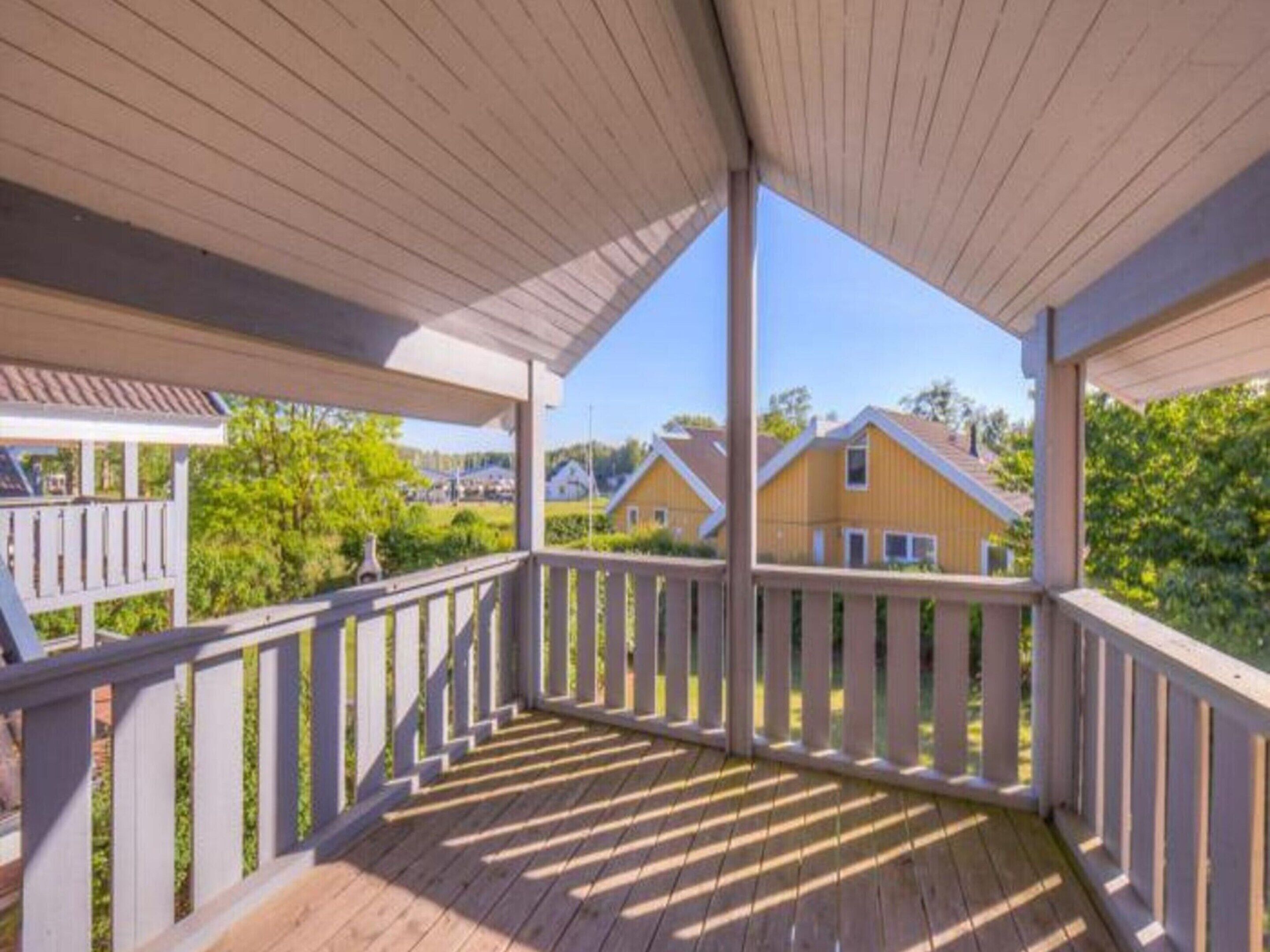 A covered wooden deck with white railings, overlooking a residential area with houses and greenery.