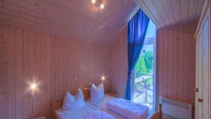 Une chambre dans une cabane en bois, avec deux lits, une table de chevet et une fenêtre avec des rideaux.