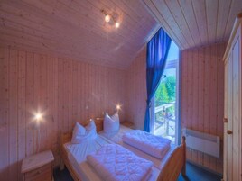 A wooden cabin bedroom with two beds, a nightstand, and a window with curtains.