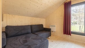 A wooden-paneled room with a gray sofa, a window with red curtains, and a white radiator. - Attractive Chalet With Terrace (Sankt Georgen am Kreischberg)