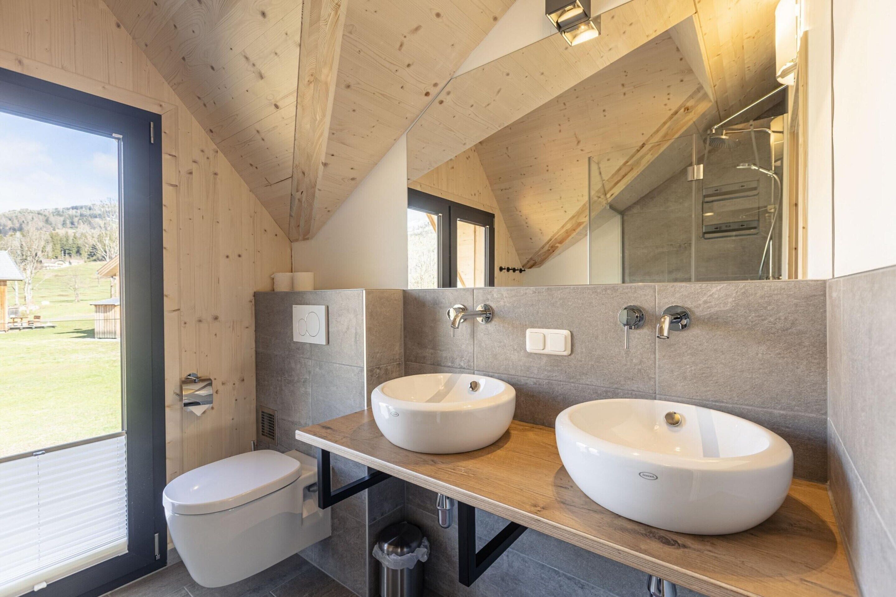A modern bathroom with wooden beams, two sinks, and a large mirror.