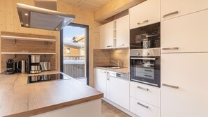 A modern kitchen with wooden cabinetry, stainless steel appliances, and a large window overlooking a snowy landscape. - Attractive Chalet With Terrace (Sankt Georgen am Kreischberg)