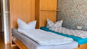 Un lit en bois avec deux oreillers et un matelas, une étagère en bois et un mur orné d’un motif.