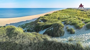 A beach with a dune, a clear sky, and a red structure on the dune. - 2 Person Holiday Home in Ulfborg (Ulfborg)