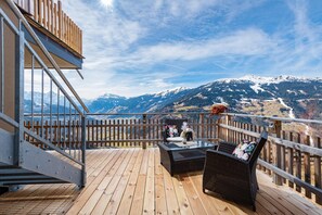 Eine HolzdTerrasse mit einem Glastisch und Korbstühlen, mit Blick auf eine gebirgige Landschaft.