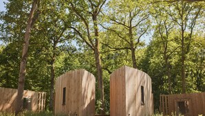 A rustic wooden cabin with a simple, open design, surrounded by lush greenery and trees. - The Brookside Escape (Antoing)