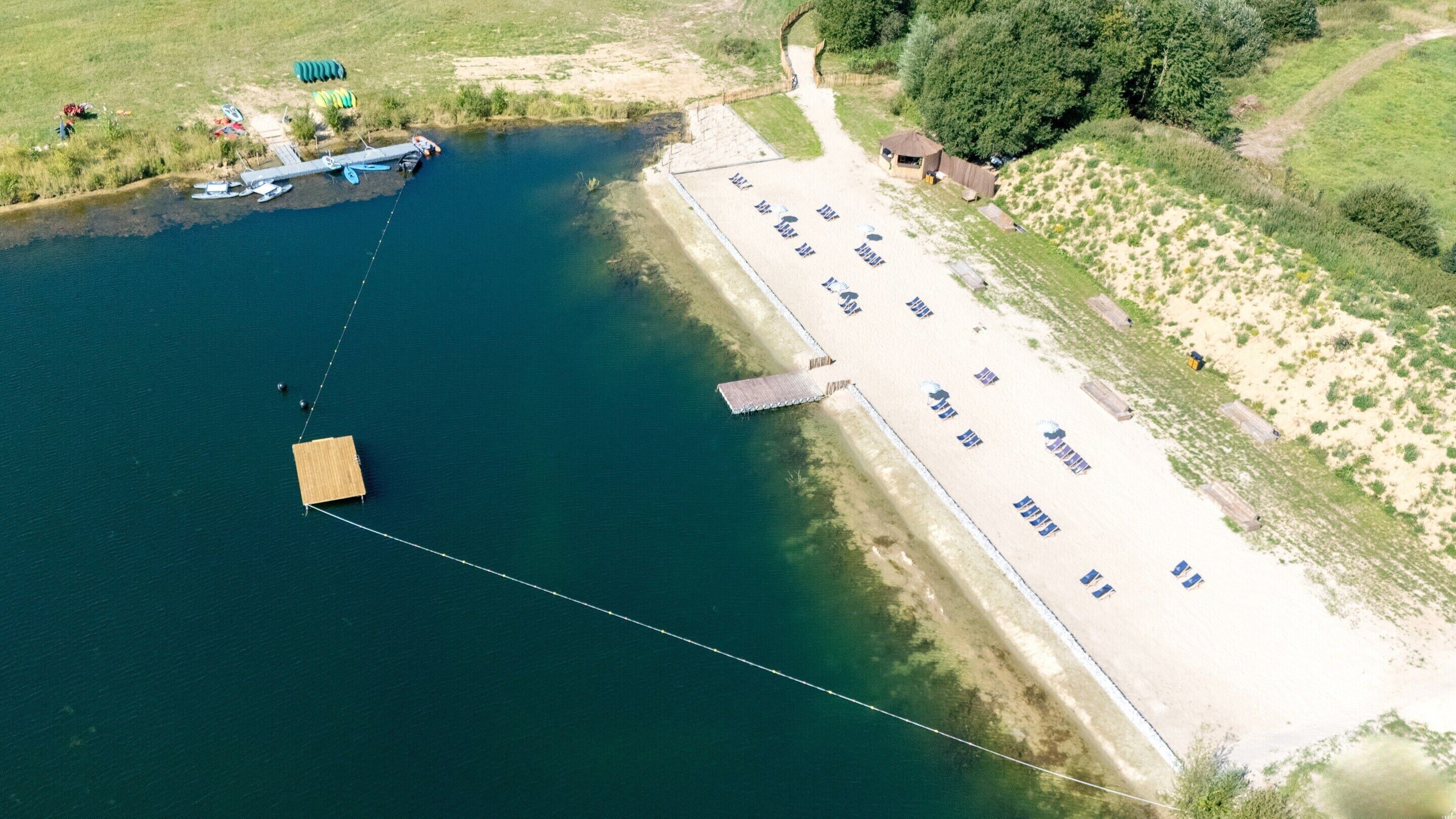 An aerial view of a lakeside property with a dock, a parking area, and a small building.