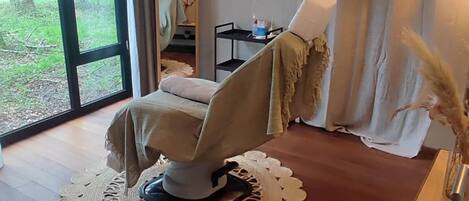 A room with a massage chair, a large mirror, and a view of greenery outside.