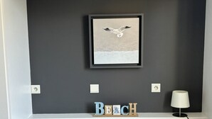 A bedroom with a dark gray wall, a framed seagull picture, and a bedside table with a lamp. - Cosy Apartment With Terrace Near Beach (Nieuwpoort)