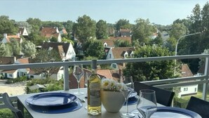 A table set for two with blue plates and wine glasses, a bottle of white wine, and a bowl of flowers. - Cosy Apartment With Terrace Near Beach (Nieuwpoort)