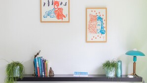 A living room with a fireplace, a bookshelf with books and decorative items, two framed artworks, and a teal lamp on a shelf. - Nice Holiday Home Near Beach (Wemeldinge)