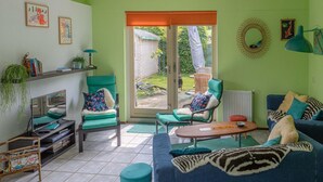 A living room with a sofa, chairs, a coffee table, and a TV. There is a bookshelf with books and a plant. The room has a large window and a door leading outside. - Nice Holiday Home Near Beach (Wemeldinge)