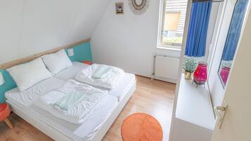 Een slaapkamer met een bed, een raam met gordijnen, een radiator en een klein oranje vloerkleed.