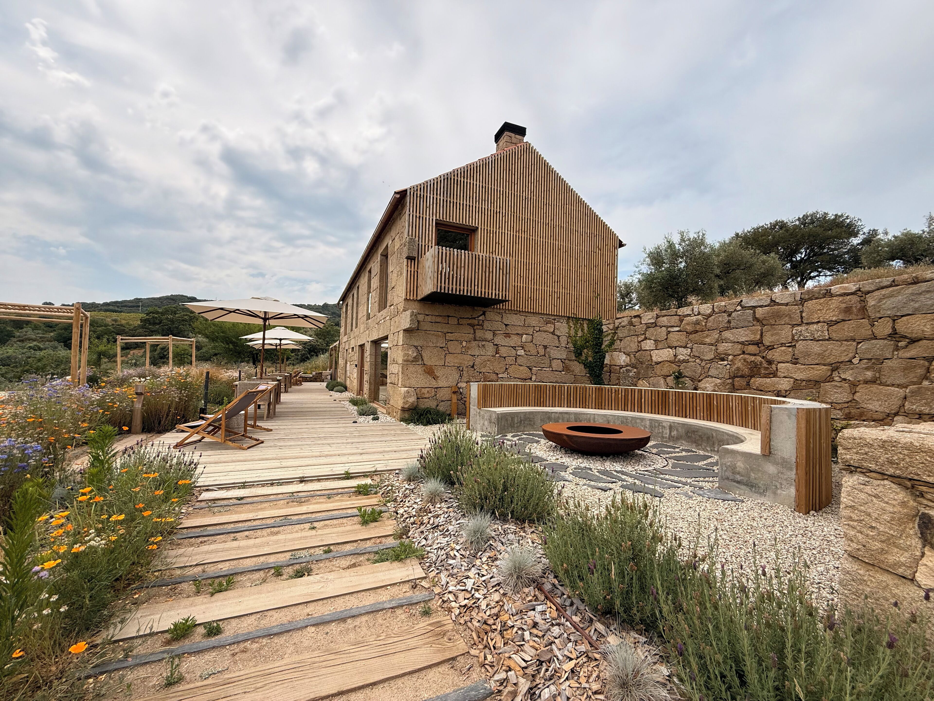 A rustic stone building with a wooden deck leading to a seating area with umbrellas.