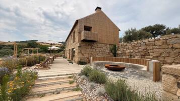 A rustic stone building with a wooden deck leading to a seating area with umbrellas.