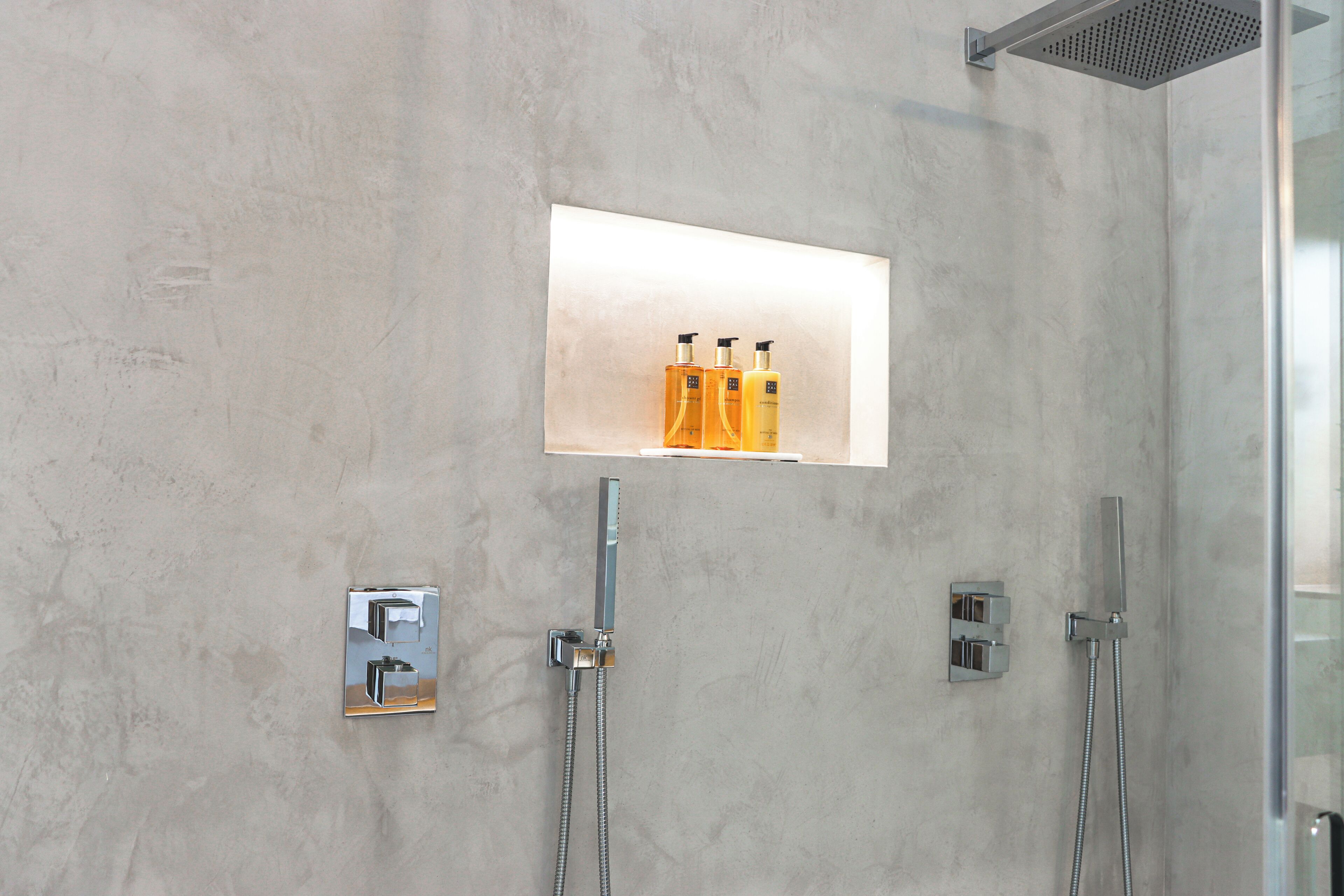 A modern bathroom with a shower, a mirror, and a shelf with toiletries.