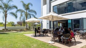 An outdoor patio area with tables and chairs, umbrellas, and palm trees. - Stylish & Elegant With Epic Views Near Menlyn (Pretoria)