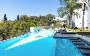 A swimming pool with lounge chairs and umbrellas, surrounded by palm trees and a view of a forested area. - Stylish & Elegant With Epic Views Near Menlyn (Pretoria)