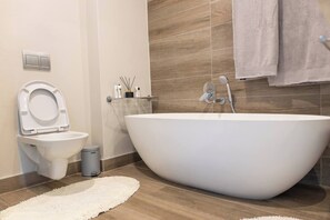 A modern bathroom with a freestanding toilet, a large bathtub, and a small trash bin. - Stylish & Elegant With Epic Views Near Menlyn (Pretoria)