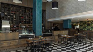 A restaurant with a checkered floor, black and white chairs, a bar area with shelves of bottles, and a counter with a person behind it. - Stylish & Elegant With Epic Views Near Menlyn (Pretoria)