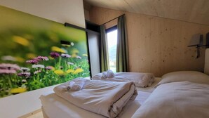 A room with two beds, each with neatly folded white towels, a large window with curtains, and a wall mural of flowers. - Beautiful Chalet With Sauna (Sankt Georgen am Kreischberg)