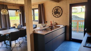 A modern kitchen with a wooden island, a dining area with a table and chairs, and a large clock on the wall. - Beautiful Chalet With Sauna (Sankt Georgen am Kreischberg)