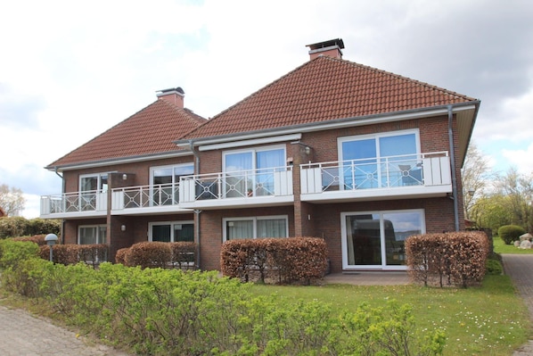 A two-story residential building with a brick facade, white-framed windows, and a balcony with a white railing.
