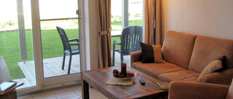 A living room with a sofa, a coffee table, and a view of a garden through a glass door.