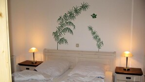 A neatly made bed with white bedding, two bedside tables with lamps, and a wall with a plant decal.