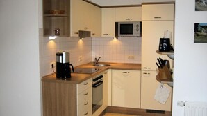 A compact kitchen with white cabinets, a microwave, a coffee maker, and a sink.