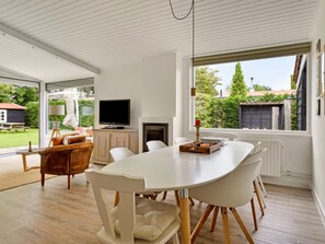 A modern dining area with a white table, chairs, and a television on a cabinet. - Holiday Home in Kamperland Near Beaches (Kamperland)