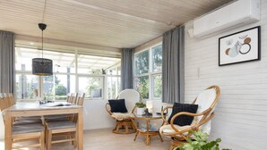 Une pièce spacieuse avec une table à manger en bois, des chaises en osier et une grande fenêtre avec des rideaux.