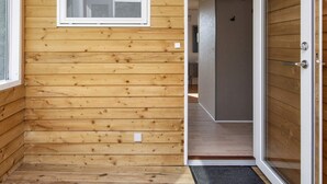 Un intérieur en bois avec une porte donnant sur une autre pièce, une petite fenêtre et un paillasson.