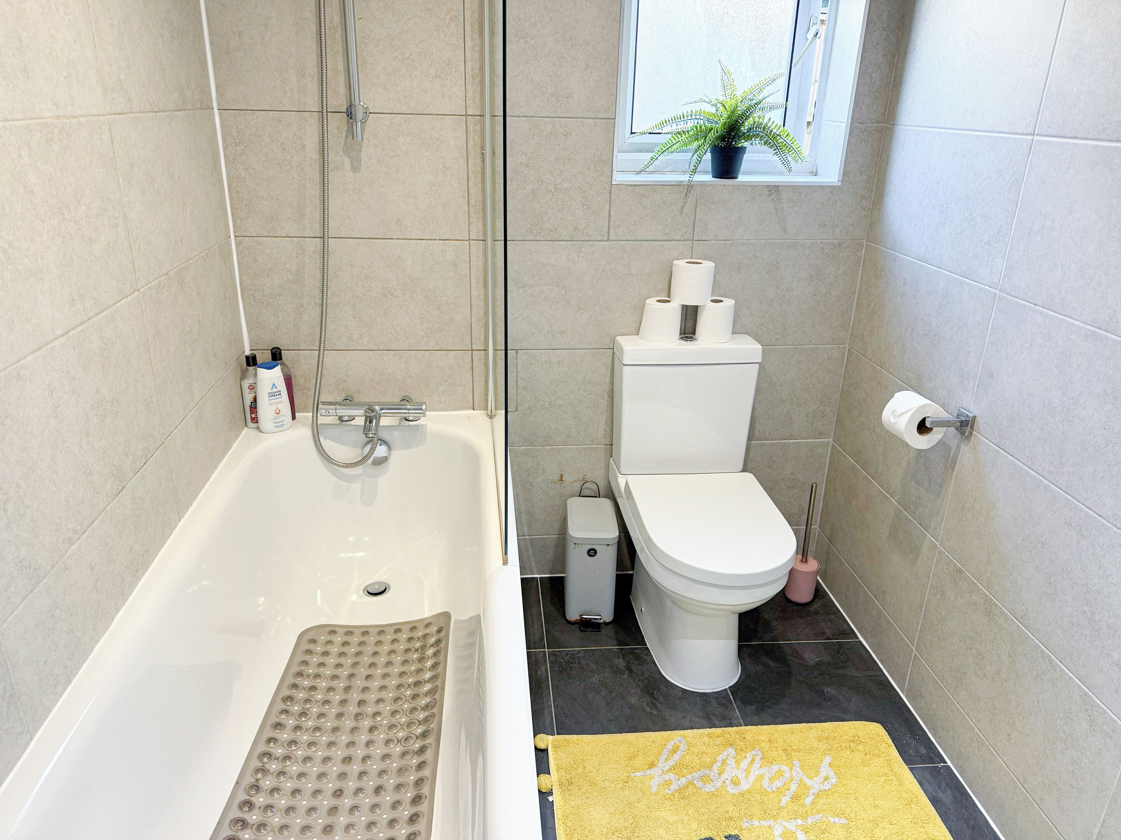 Un baño con bañera, inodoro y ventana con planta.
