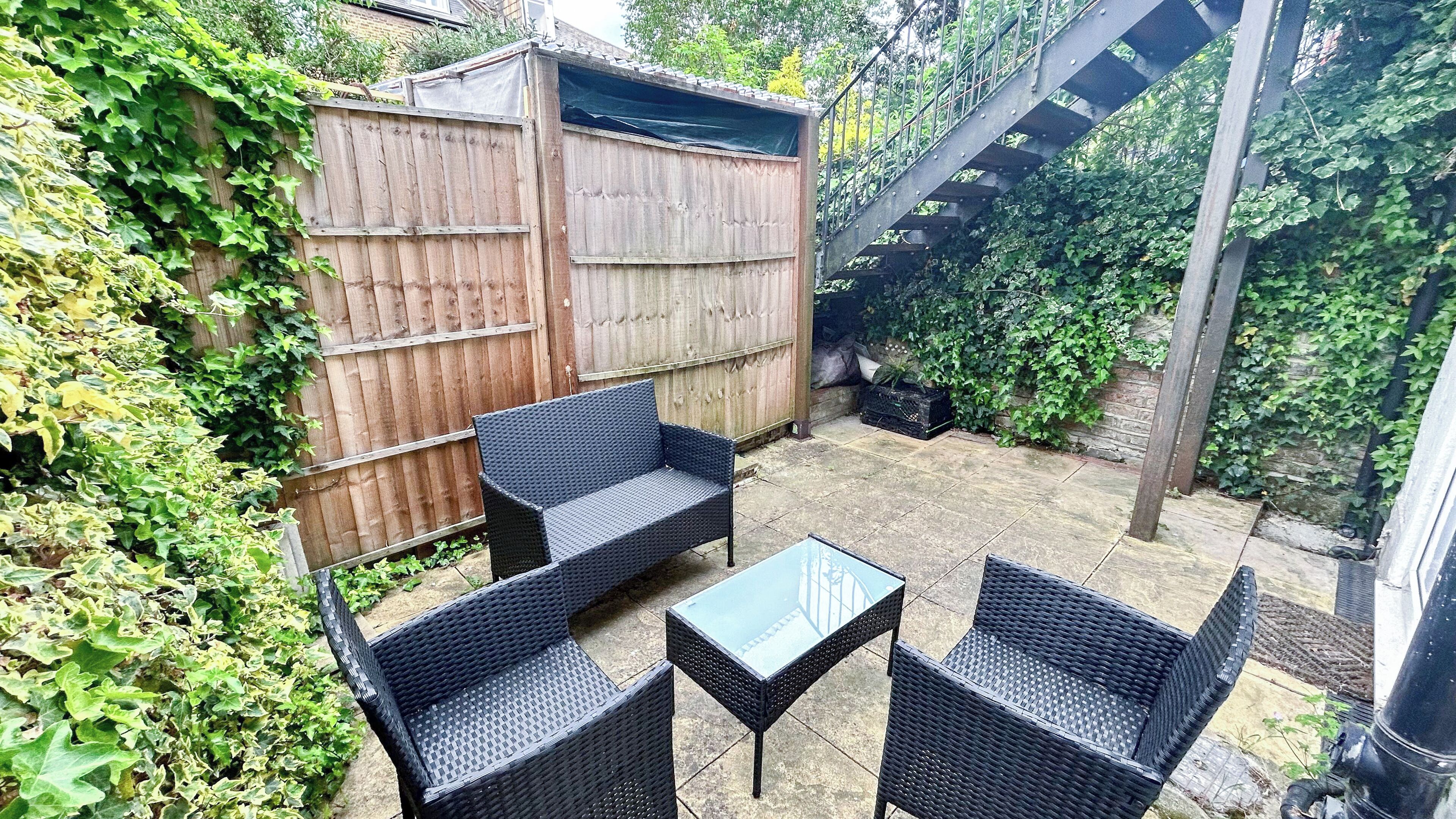 Une terrasse avec des meubles en osier, une petite table et un abri de jardin en bois.