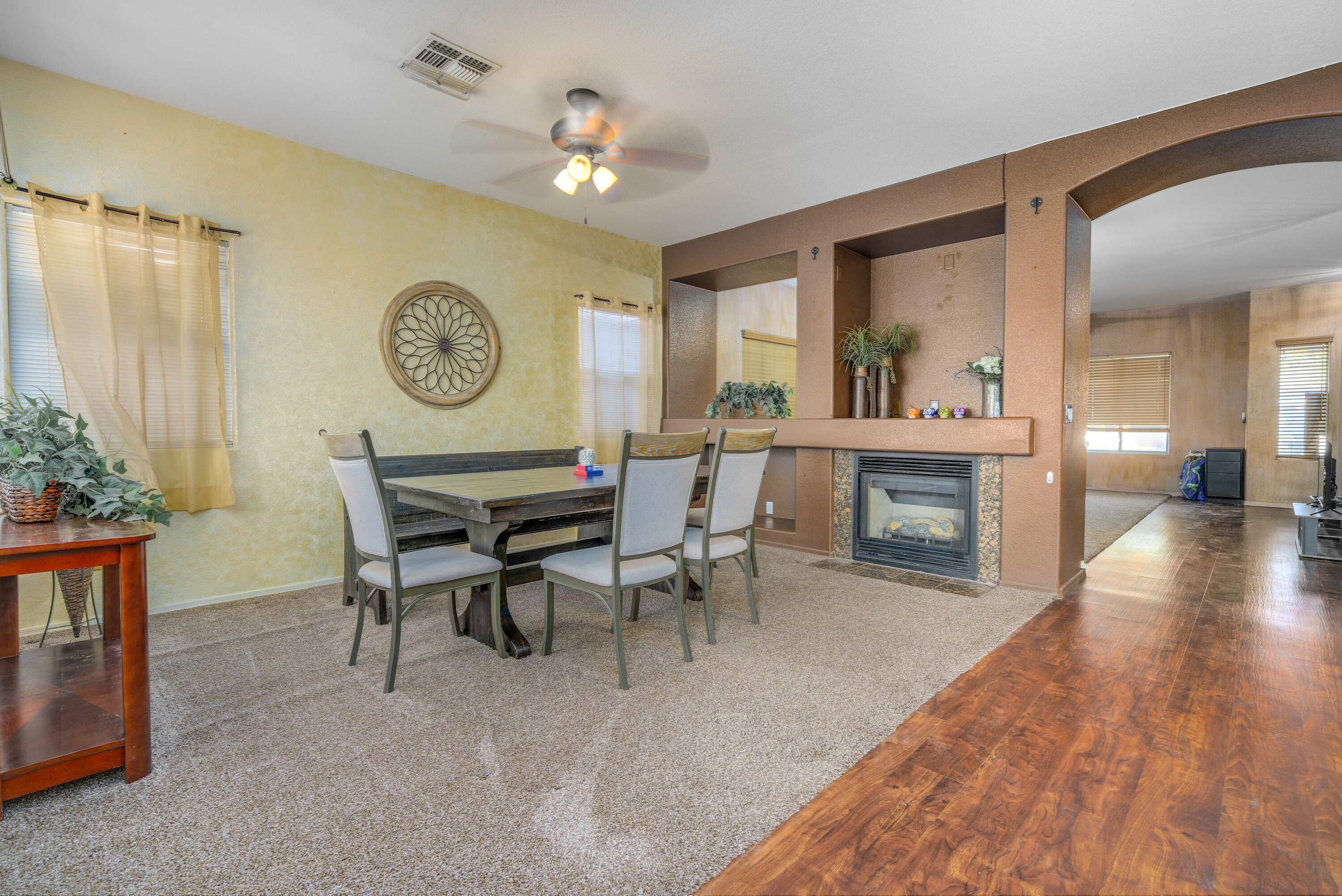 A dining area with a wooden table and chairs, a fireplace, and a ceiling fan.