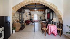 Une cuisine rustique aux murs de pierre, avec une arche en bois, un coin repas comprenant une table et des chaises, et un canapé rouge.