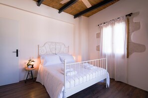 A bedroom with a white metal bed, a bedside table with a lamp, and a window with curtains. - The Fabrica Falasarna (Kissamos)