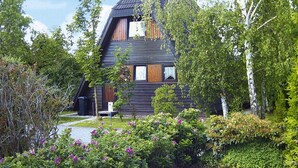Een modern houten huis met een schuin dak, omgeven door weelderig groen en bloeiende struiken.