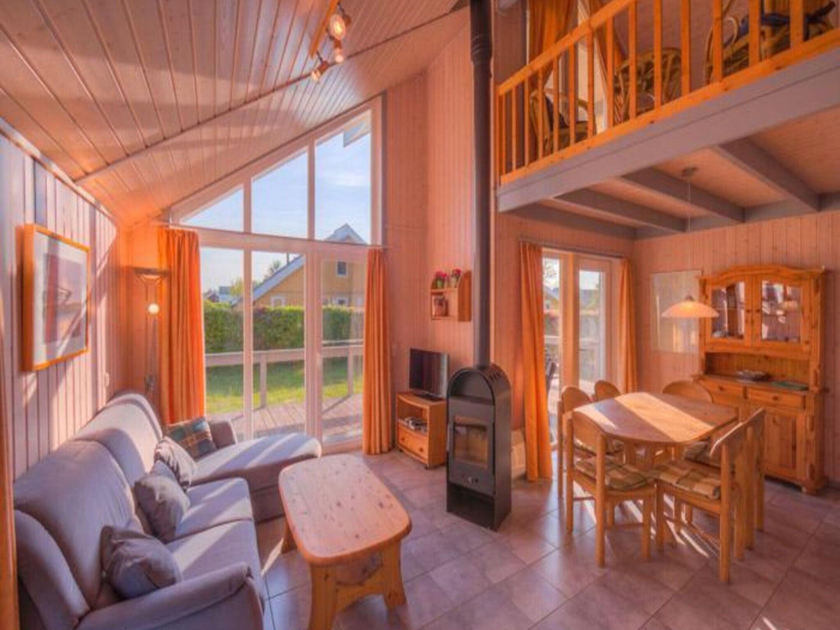 A cozy cabin interior with a sofa, a wooden table, a TV, and a dining area.
