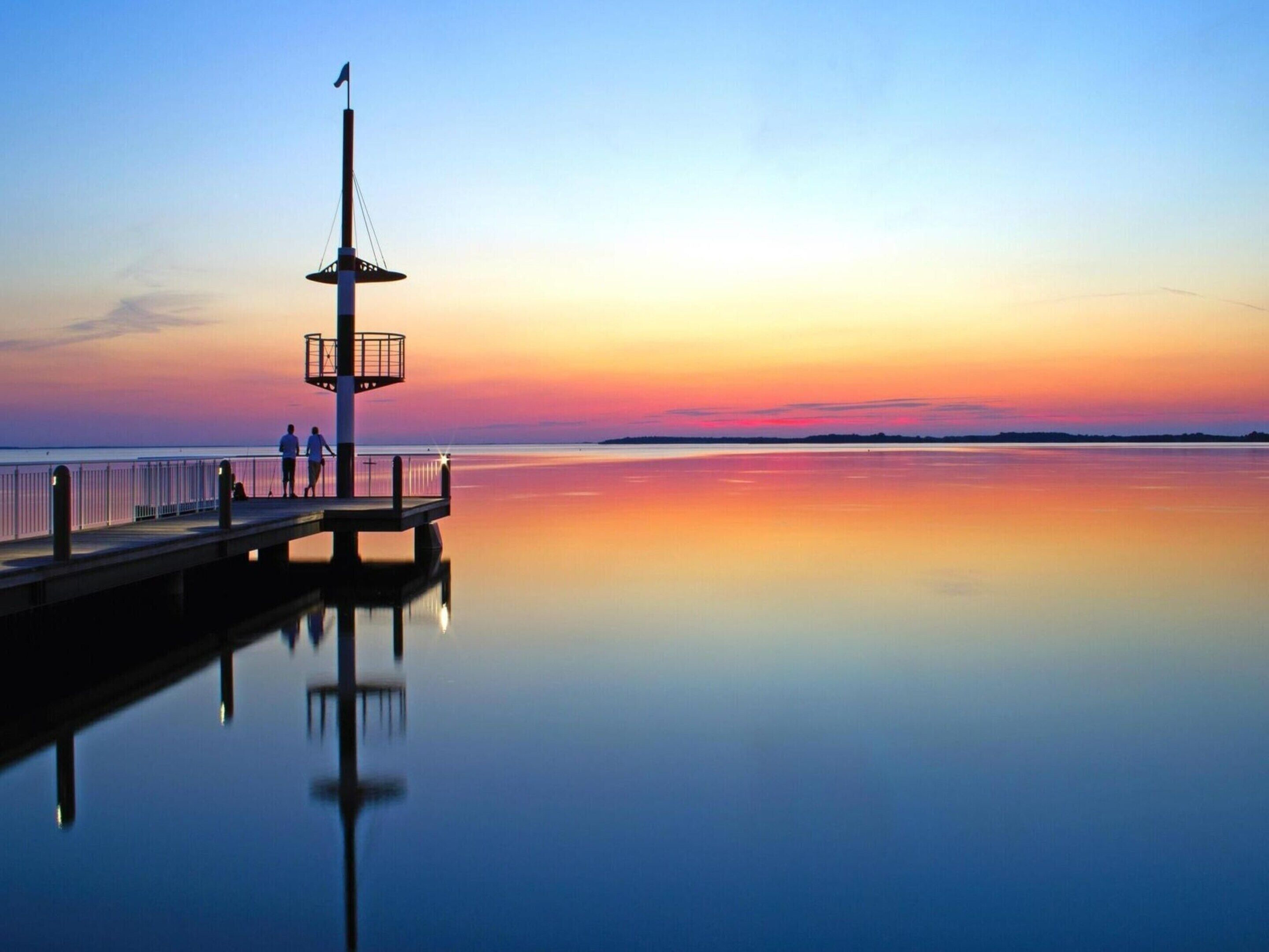 A pier extending into calm waters at sunset with a small observation tower and a flag.